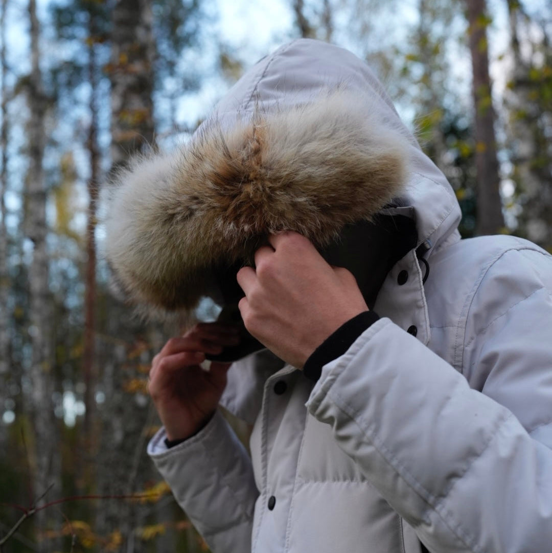 Person wearing a Canada Goose wyndham parka with a fur-lined hood in a forest setting